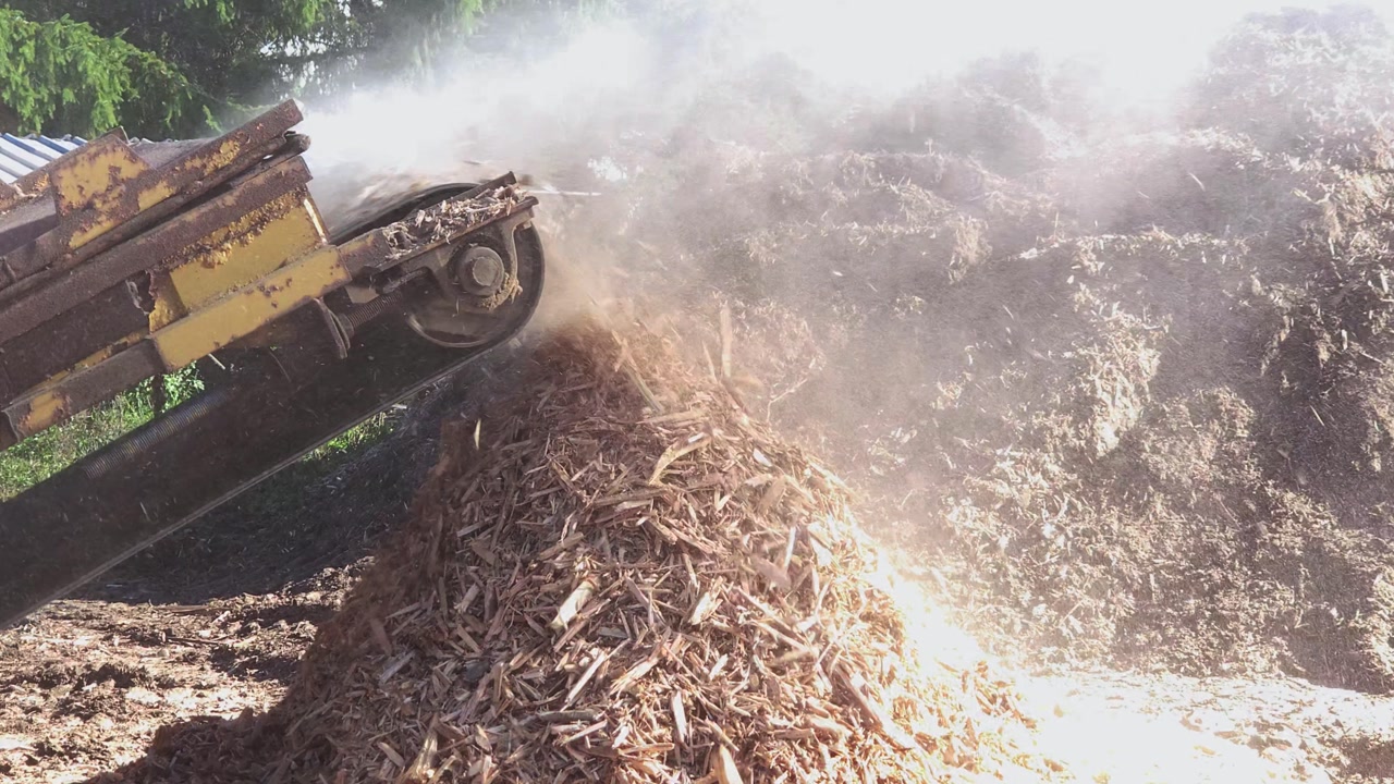 Slow motion medium shot of an industrial grinder flinging wood chips onto a pile