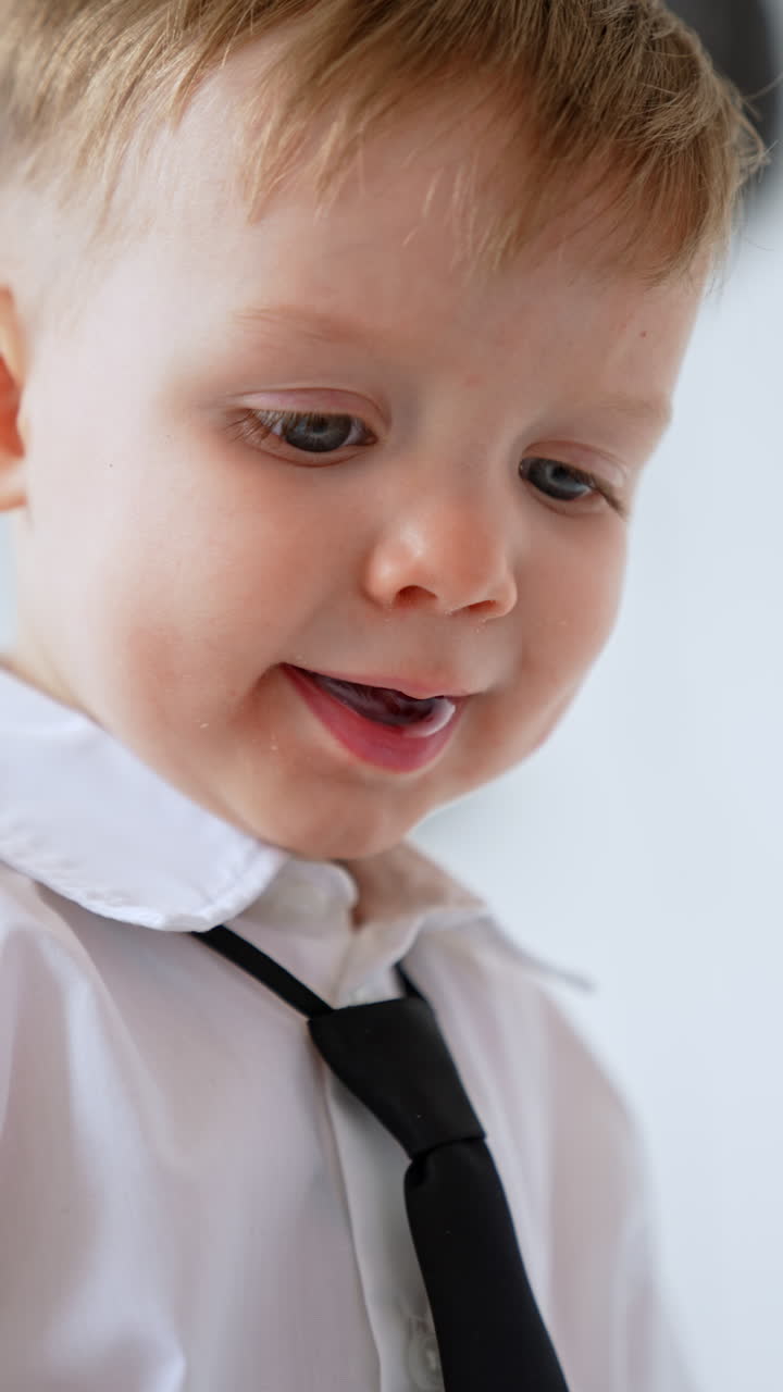 Adorable Caucasian two-year-old toddler boy wearing white shirt and black tie. Close up portrait of a cute baby. Vertical video.