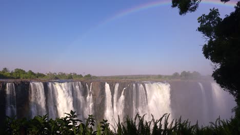 hermoso tiro de establecimiento con el arco iris sobre las cataratas victoria desde el lado de zimbabwe de la cascada africana