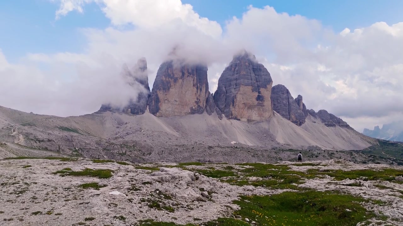 Il drone si avvicina e si inclina verso l'alto, riprendendo un viaggiatore solitario che cammina verso le Dolomiti.