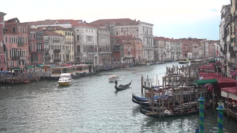 a gondolier navigating in a gondola through the grand canal of venice, viewed from the rialto bridge