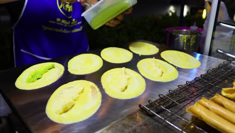 a street vendor prepares traditional thai crispy pancakes at night in bangkok. vibrant lighting highlights the meticulous cooking process