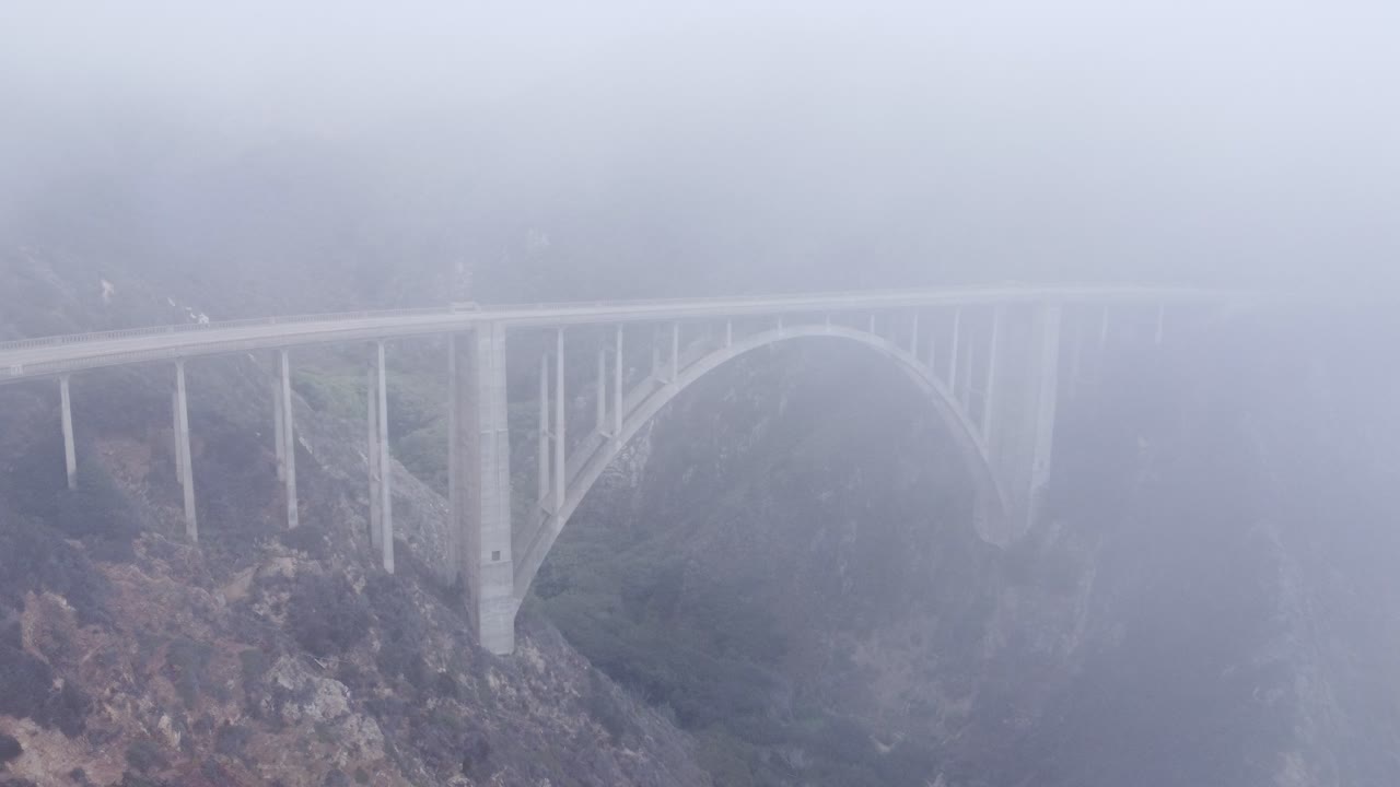 A drone fly's over a foggy bridge
