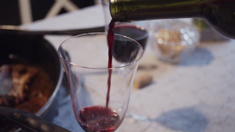 Pouring-red-wine-from-bottle-into-wineglass-on-homely-dinner-table,-closeup