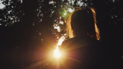 Silhouette-Eines-Mädchens,-Das-Den-Sonnenuntergang-Im-Park-Betrachtet,-Die-Sonne-Beleuchtet-Wunderschön-Ihr-Blondes-Haar