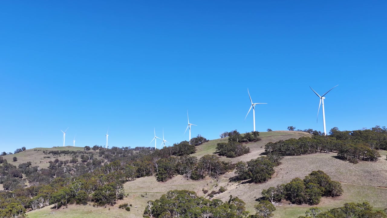 Turbine eoliche che ruotano su un pendio erboso sotto un cielo azzurro e limpido
