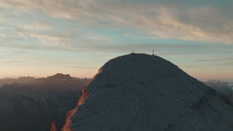 widok drona alpinisty na grzbiecie tofana di rozes we włoskich dolomitach o wschodzie słońca, z widocznym w tle krzyżem szczytu i monte antelao