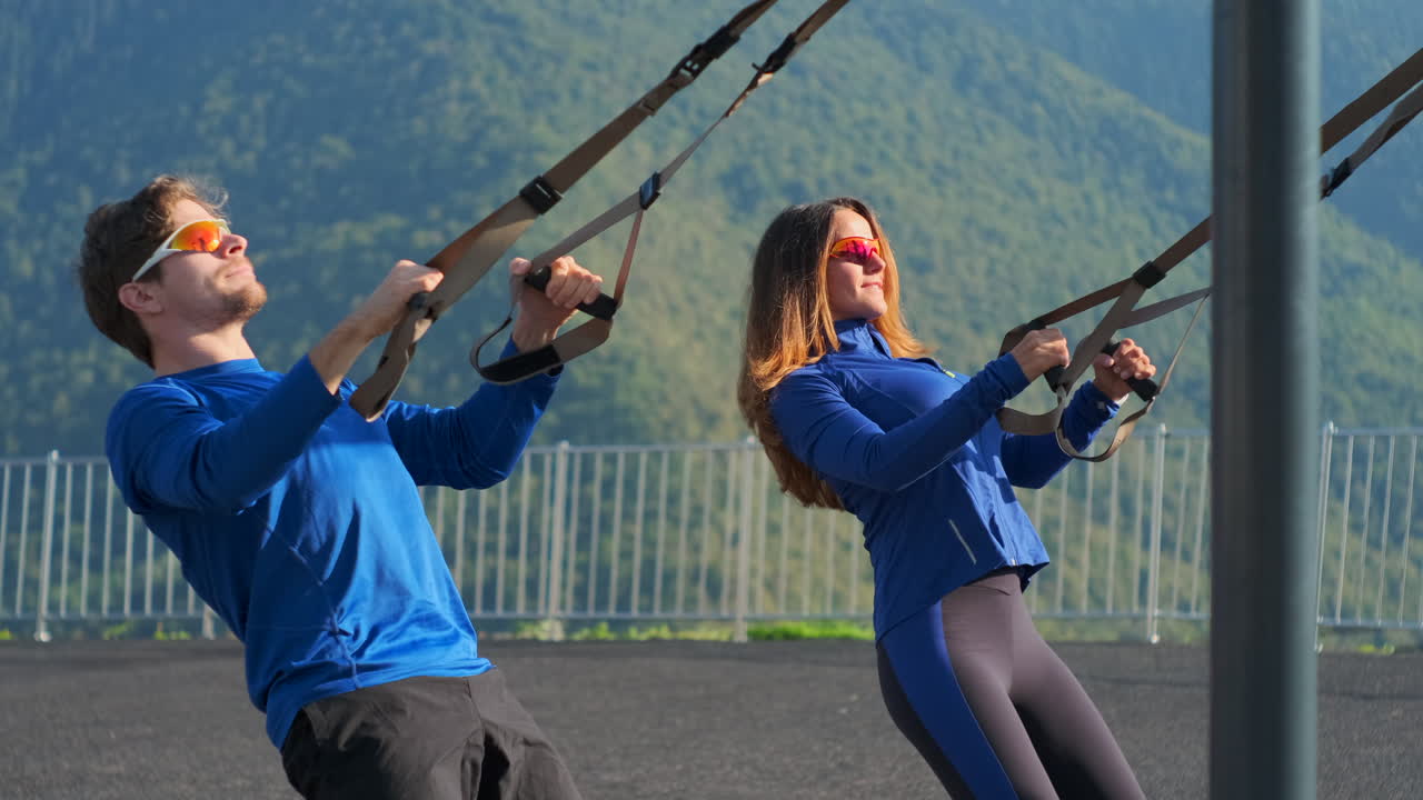 커플이 야외에서 서스펜션 훈련 장비로 운동하고 있습니다.