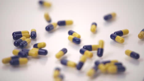 slow motion macro of blue and yellow pills dropped onto white background