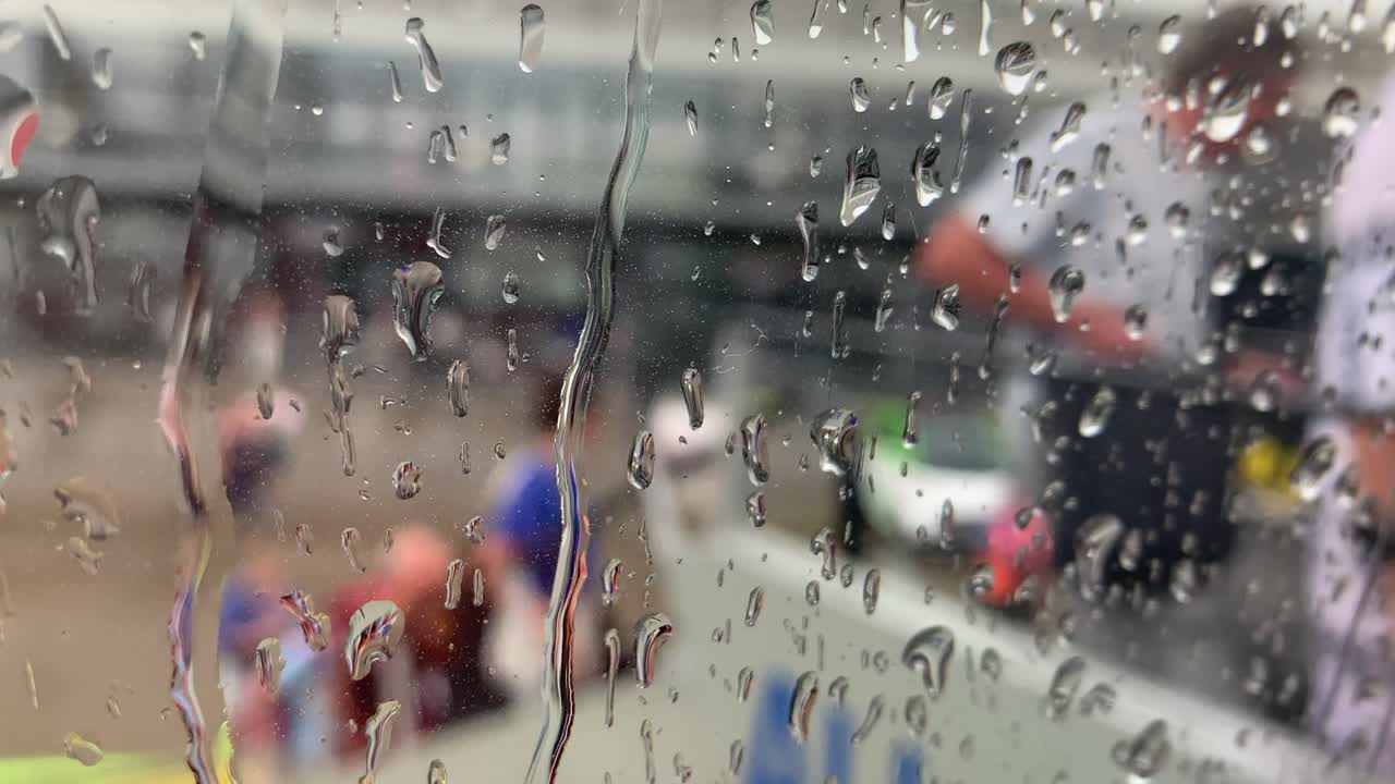 Raindrops gently slide and glide across the airplane window, blurring the view outside, with unrecognizable figures in the background adding a serene, atmospheric effect.