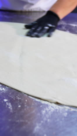 cook's gloved hand spreads flour over the metal table. rolled out white dough lies on the table for future cooking. close up. vertical video