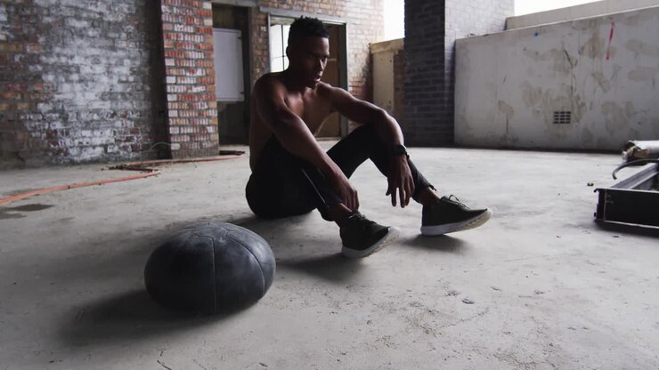 African american man sitting resting after exercising with medicine ball in an empty urban building
