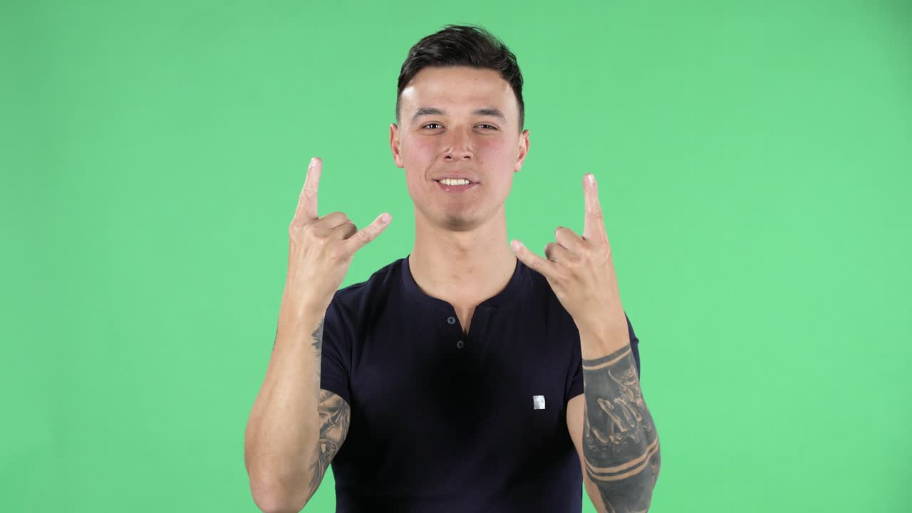 retrato de un joven guapo está mirando a la cámara y haciendo un gesto de roca y disfrutando de la vida. pantalla verde