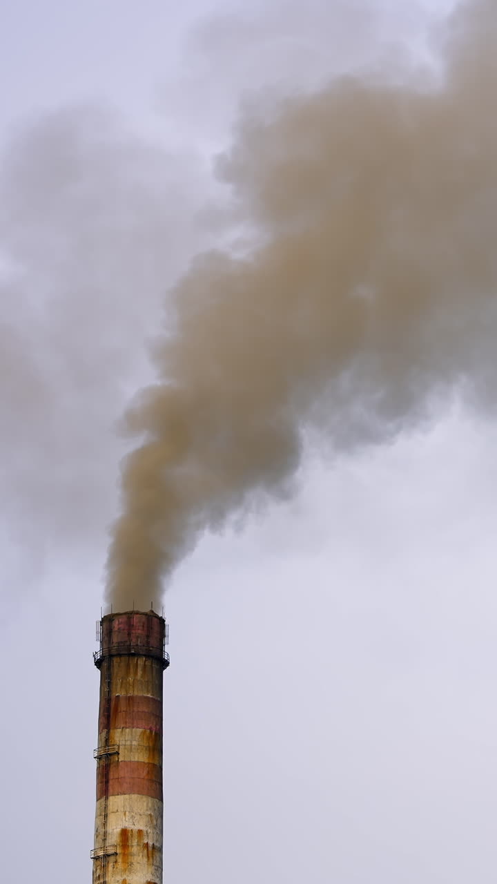 Pollution by industrial production. Fuming pipe power plant against the cloudy sky. Vertical video