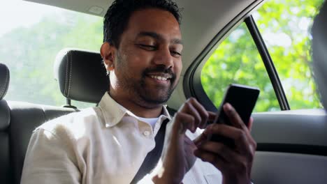 Pasajero-Masculino-Llamando-Por-Teléfono-Inteligente-En-Un-Taxi.-Concepto-De-Transporte,-Negocios-Y-Tecnología.-Feliz-Y-Sonriente-Pasajero-Indio-O-Empresario-Usando-Una-Grabadora-De-Comandos-De-Voz-En-Un-Teléfono-Inteligente-En-El-Asiento-Trasero-De-Un-Taxi.