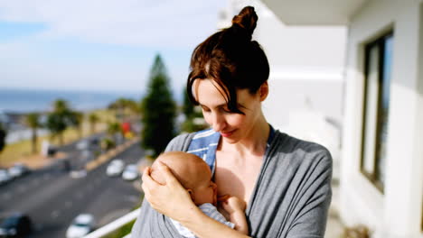 young smiling mother standing in balcony with baby in sling 4k