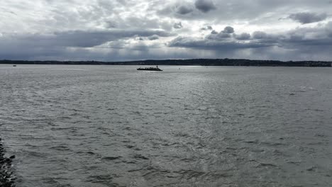 An-aerial-view-of-a-barge-and-a-ferry-in-the-distance,-sailing-in-Upper-Bay,-New-York-on-a-cloudy-day