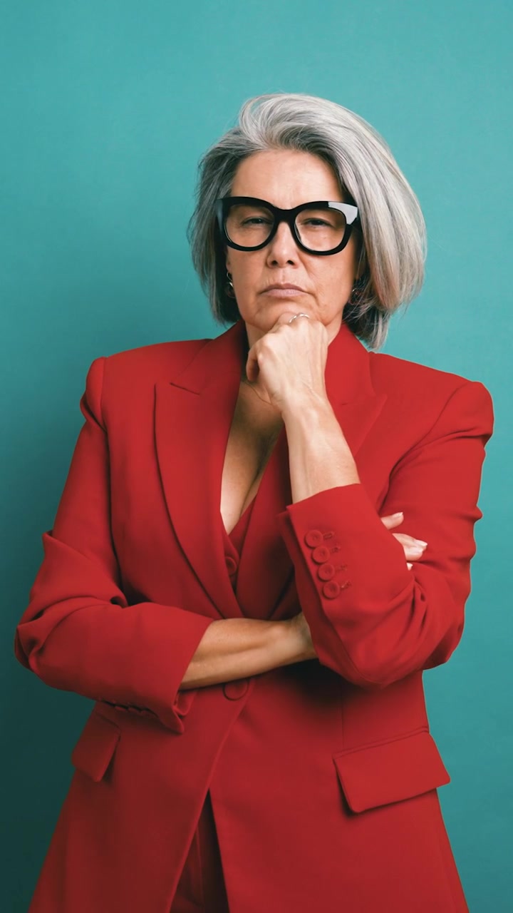 Donna matura seria in blazer rosso che gesticola e pensa
