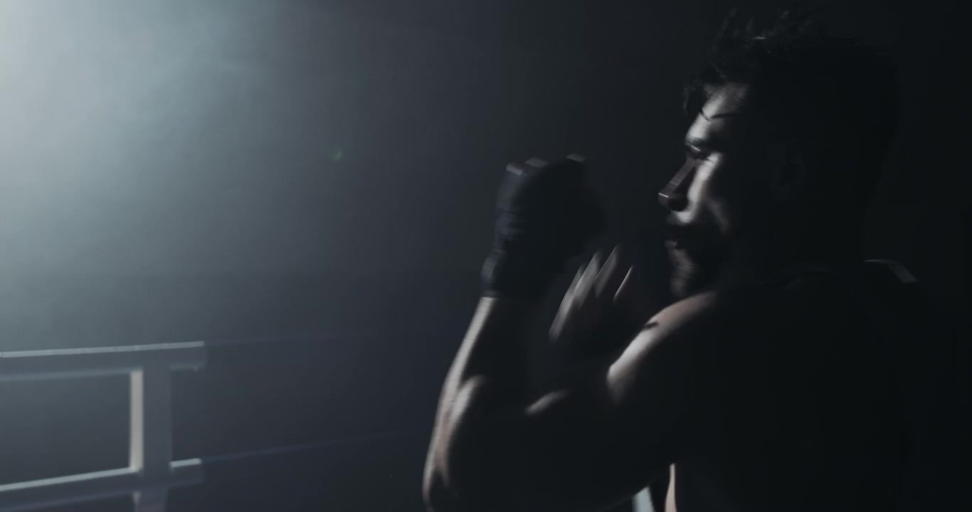 Silhouette di un pugile che fa shadow boxing in un ring buio e fumoso.