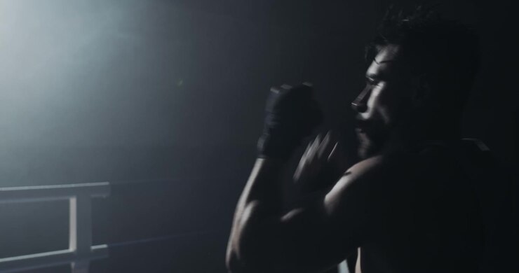 Silhouette di un pugile che fa shadow boxing in un ring buio e fumoso.