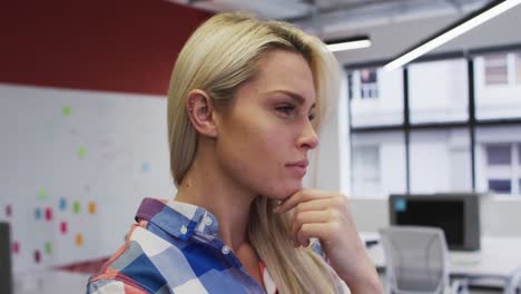 Caucasian-businesswoman-rubbing-her-chin-in-thought-and-smiling-in-office