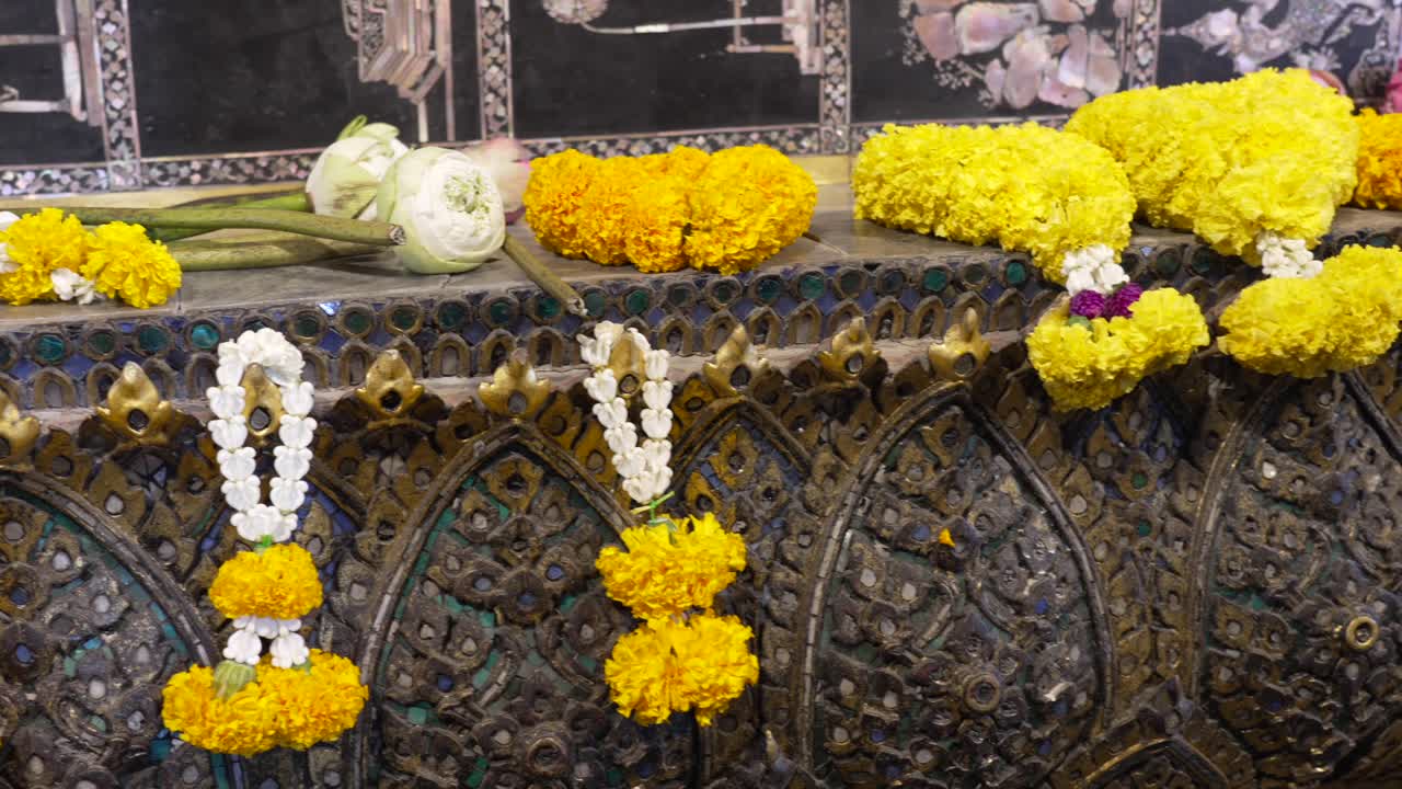 Ghirlande colorate di calendule e fiori di loto e boccioli deposti su una balaustra dorata e decorata dell'altare al Wat Pho, Bangkok, come offerte floreali di devozione e riverenza spirituale, ripresa al rallentatore