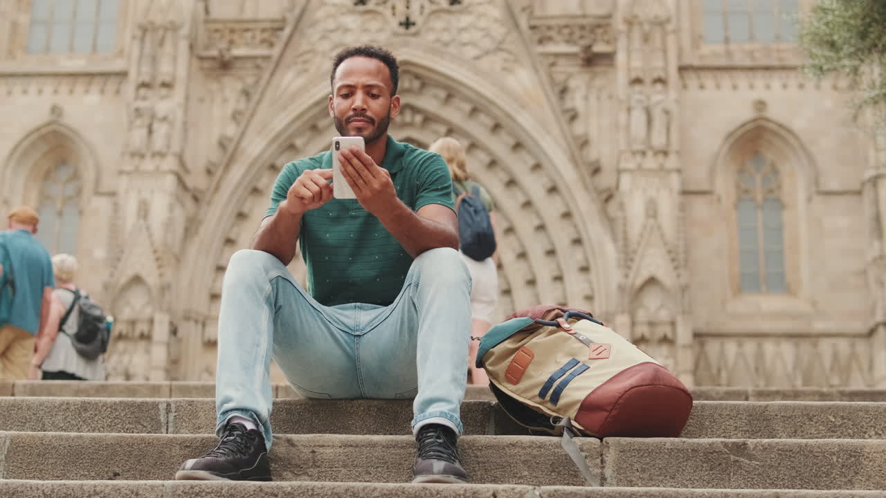 Uomo con smartphone seduto sulle scale di fronte alla cattedrale