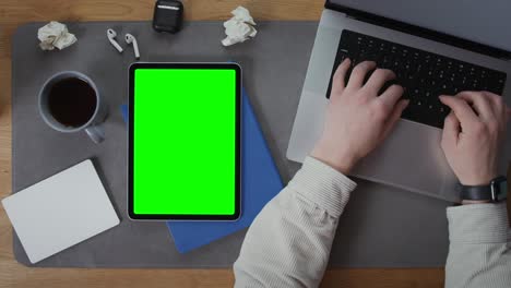 persona que trabaja en una computadora portátil y una tableta con pantalla verde