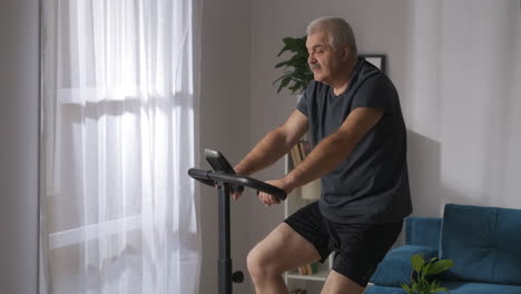 Un-Hombre-Adulto-Está-Perdiendo-Entrenamiento-Con-Pesas-En-Una-Bicicleta-De-Ejercicio-En-Una-Actividad-Deportiva-En-Casa-En-Un-Autoaislamiento-En-Un-Estilo-De-Vida-Saludable-Pandémico