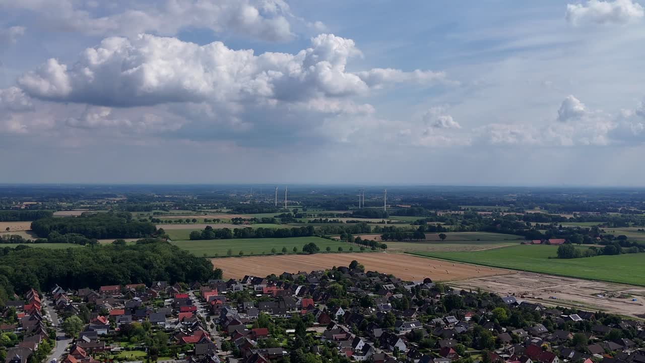 Quiet rural neighborhood of USA with wind turbines on agricultural farm fields. Aerial wide shot. Puffy clouds at sky. Houses and homes of small American town. Summer day season