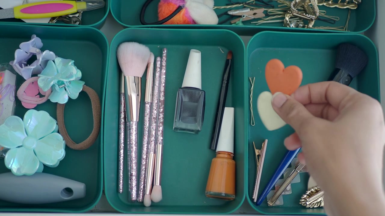 Mano che prende fermagli per capelli a forma di cuore da un cassetto di bellezza organizzato