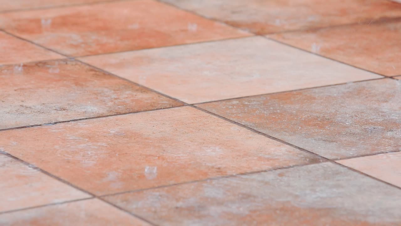 Detail of raindrops hitting the ground in slow motion over rustic ceramic tiles