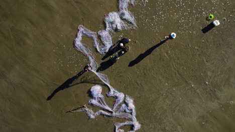 los pescadores locales en la playa sacuden los peces de la red blanca, los recogen