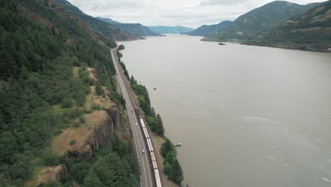 aerial rise above train and highway traffic traveling next to columbia river