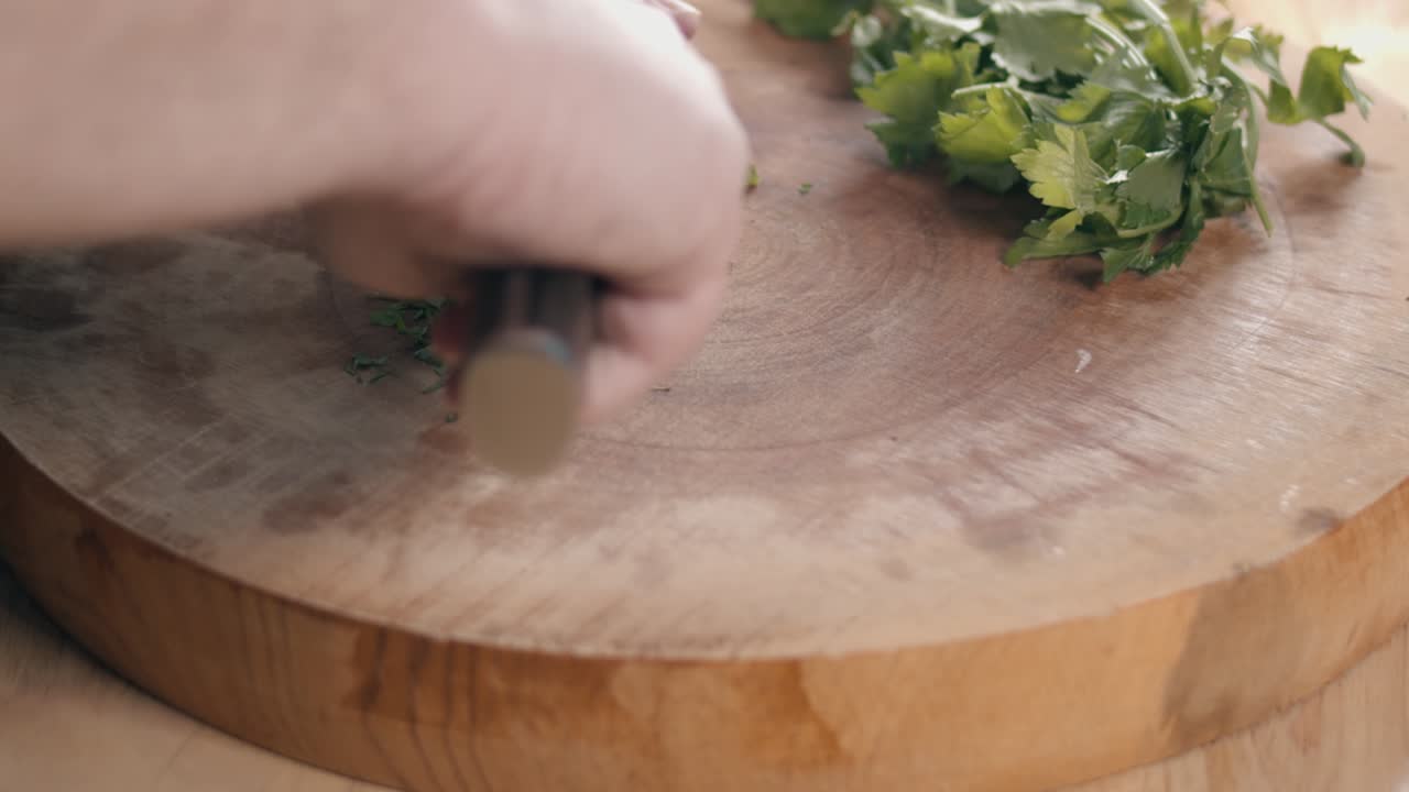 Close Slider Slow Motion Shot of Chef Hands Chopping Parsley With a Chefs Knife on a Thick Circular Wooden Chopping Board