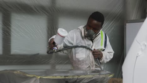 African-American-male-car-mechanic-with-a-suit-and-painting-a-piece-of-a-car-with-a-spraying-gun-