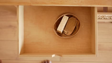 person opening a wooden drawer containing natural hair and body brushes and soap