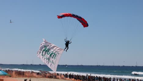 parachutists descend with banners at crowded beach