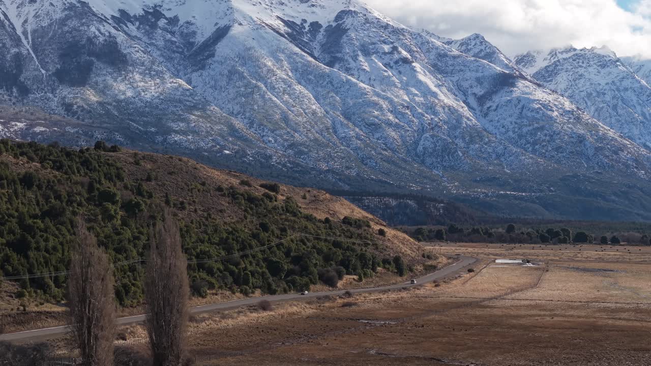 Un drone sorvola la Ruta Provincial 71, rivelando una strada tortuosa attraverso valli aride e le Ande innevate, incorniciate da alberi di lenga nativi, erbe della steppa e la bellezza aspra di Los Alerces. Campo lunghissimo
