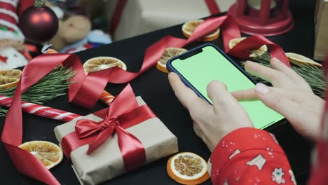 phone with green screen on table. female fingers are watching christmas presents online on cell phone with green screen. chromakey screen. hands using smartphone with green screen