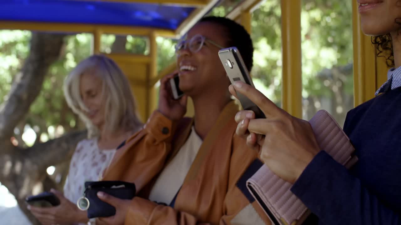 viajeras que usan teléfonos móviles en la parada de autobús 4k