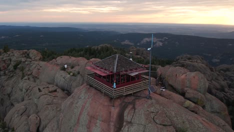 Aerial-View-of-Woman-Walking-on-360-Degrees-Platform-Around-Fire-Spotting-Building-on-Top-of-Hill