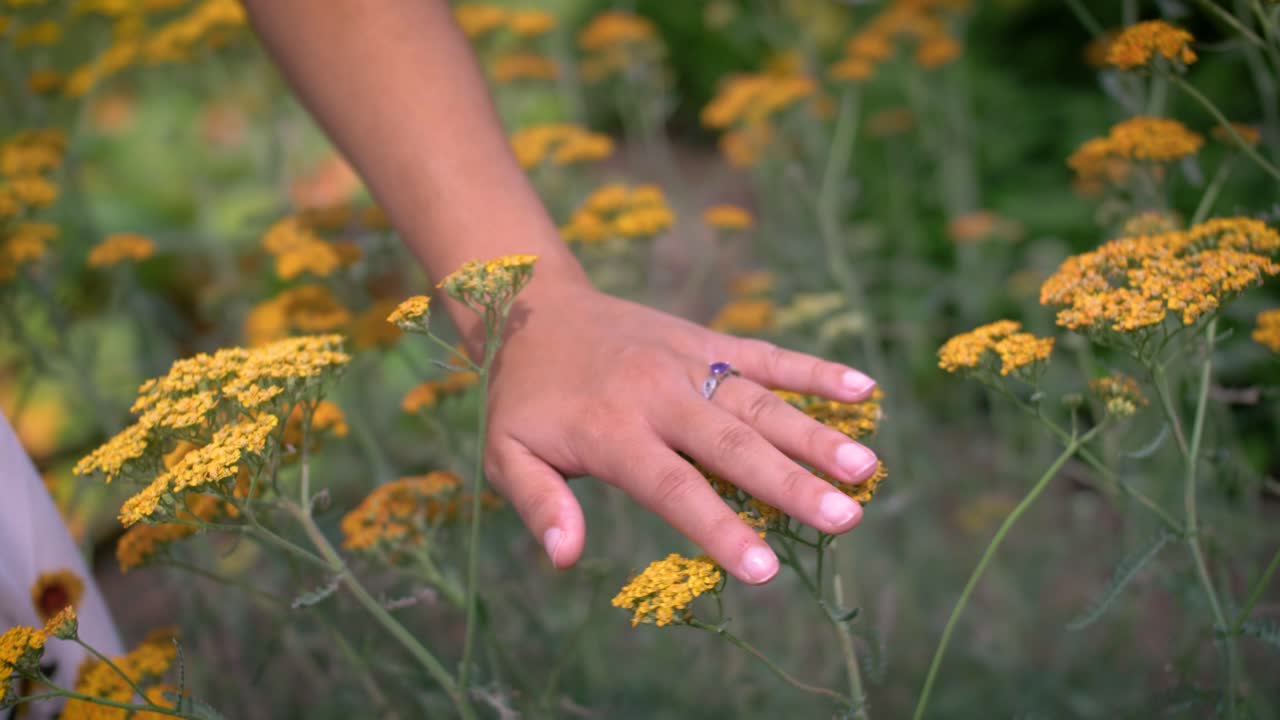 una linda chica moviendo su mano a través de flores y plantas en un brillante día de verano