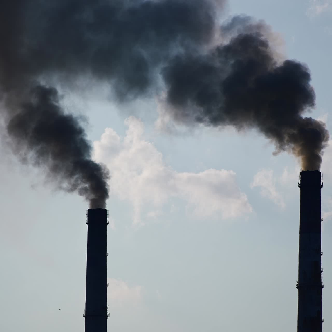 Two factory chimney pipes producing heavy dark smoke. Industry polluting the atmosphere. Cloudy sky backdrop