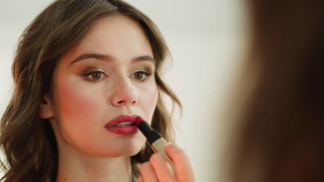 focused young woman paints lips with glamorous red lipstick