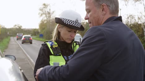 female traffic police officer takes statement from driver on mobile phone at road traffic accident