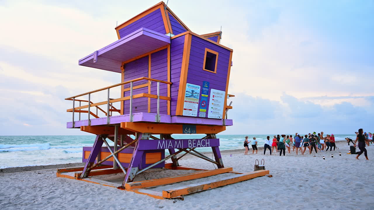 Miami, EE. UU., 16 de abril de 2026: Torre de salvavidas púrpura en Miami Beach con gente haciendo ejercicio. Icónico puesto de salvavidas colorido en la arena con clase de fitness grupal al atardecer en Florida