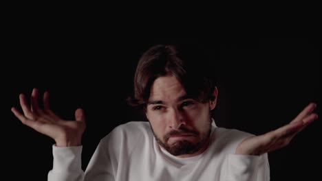 trendy young man making unsure gesture, shoulder shrug, close, black background