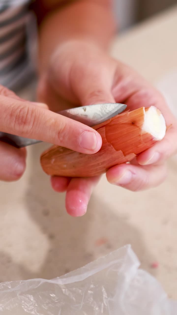 Hands peeling shallots on a kitchen counter with soft lighting, highlighting the preparation process