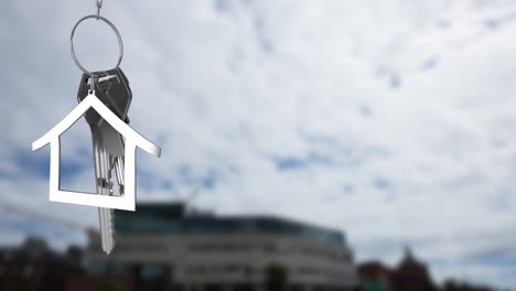 Animación-Del-Modelo-De-Casa-Plateada-Y-La-Llave-Sobre-Un-Edificio-Desenfocado-Contra-El-Cielo-Nublado